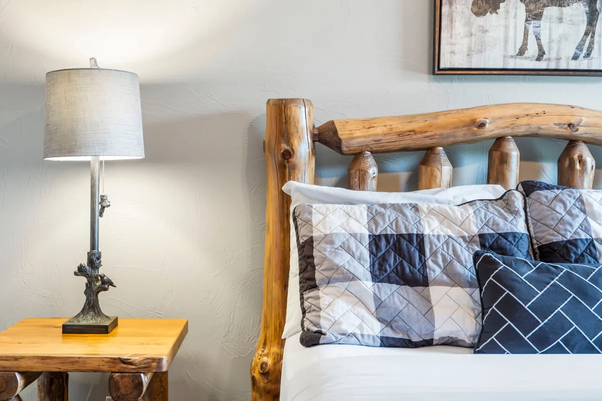 A warmly lit bedroom featuring a rustic log bed frame, quilted pillows, and a bedside table lamp. The space exudes comfort and a touch of cabin luxury, inviting quiet relaxation and restful sleep.