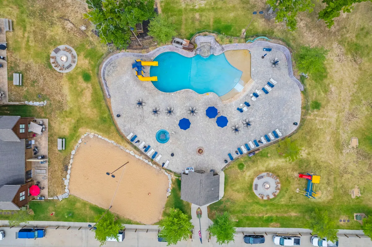 This vibrant exterior scene features the resort's swimming pool with a water slide, a sand volleyball court, a welcoming outdoor seating area, a cozy fire pit, and kids playing on the playground. The image captures multiple amenities in one frame, including spaces for swimming, games, and evening gatherings.