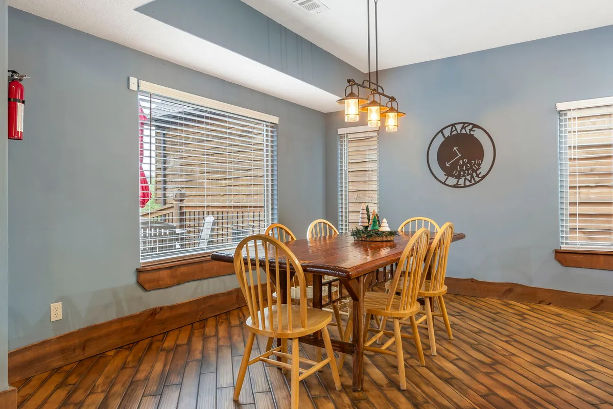 An inviting dining area is centered around a wooden dining table, illuminated by a charming light fixture and accented with lake-themed wall art. The space feels intimate and perfect for family breakfasts or evening gatherings.
